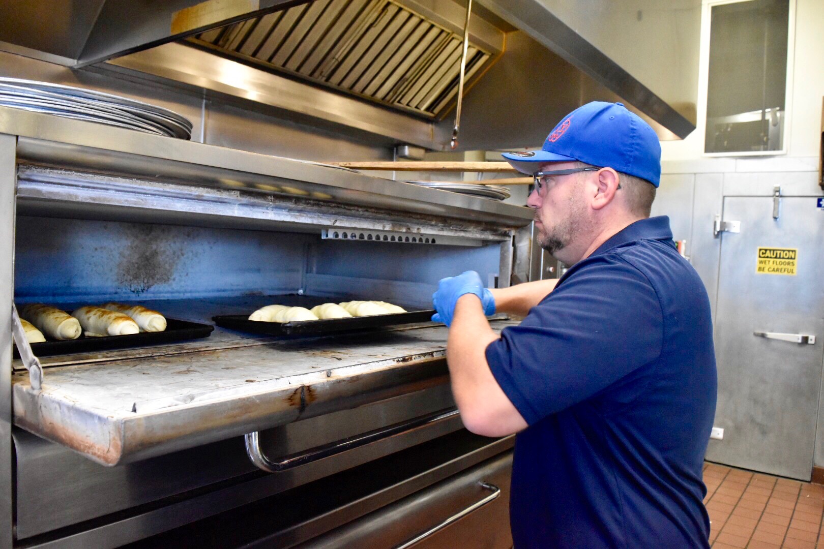 Photo of a man placing bread rolls into an oven